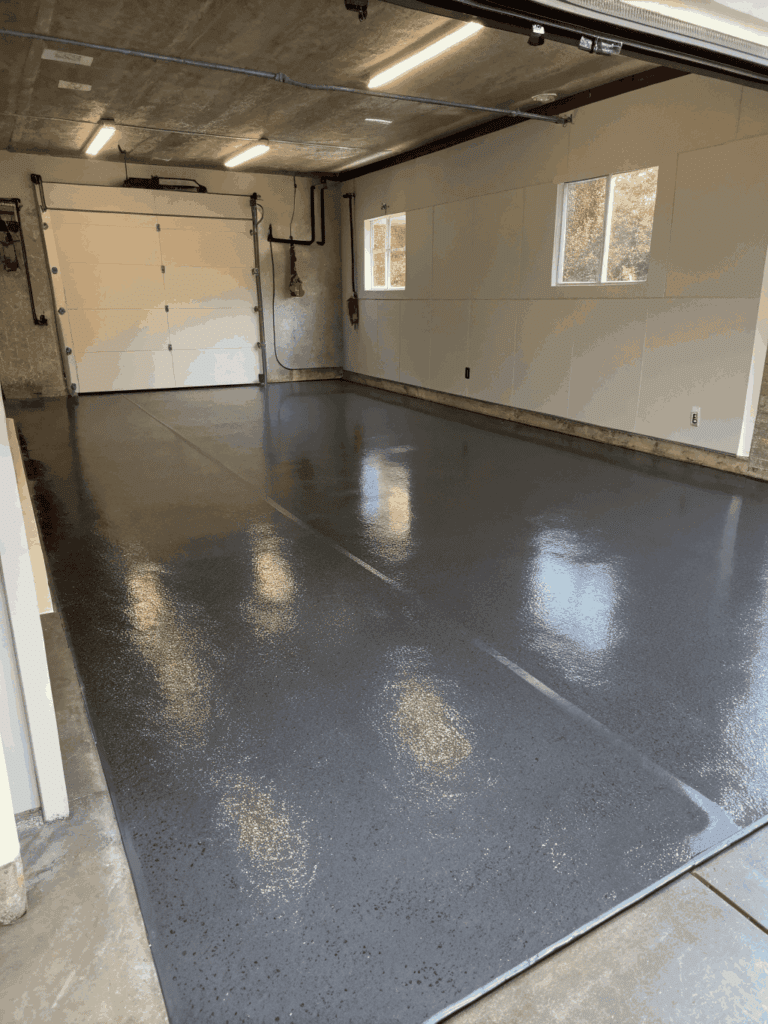 Modern garage floor with a glossy epoxy coating and a faint blue tint, with a toolbox and work gloves resting on the floor